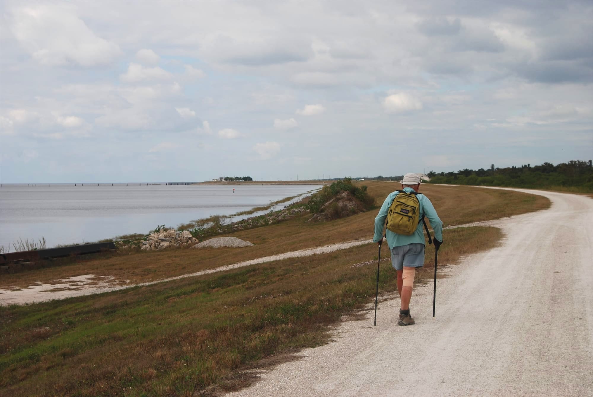 Man with hiking sticks on gravel road next to lake