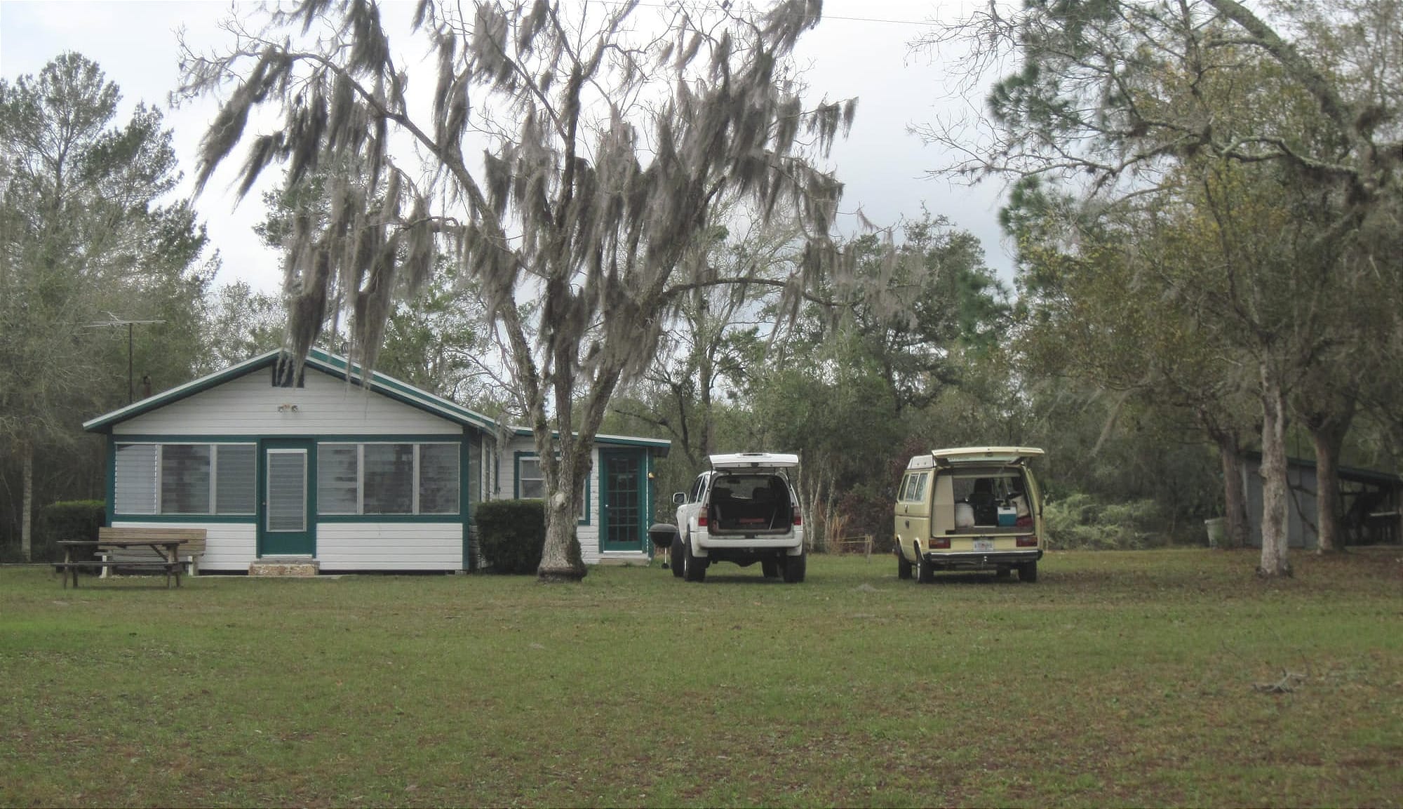 Small white cabin with green trim with an SUV and Westfalia next to it