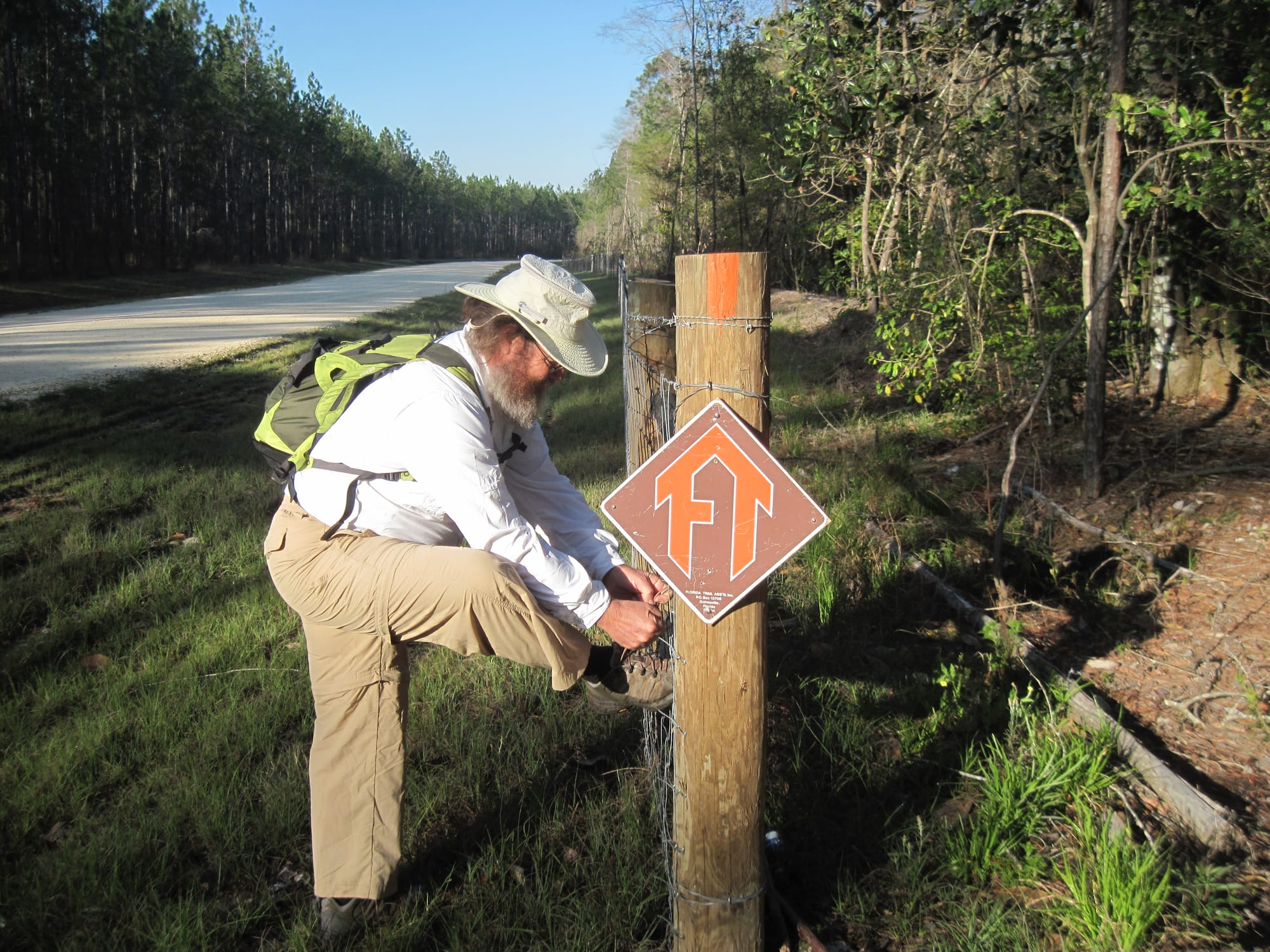 Man tying his shoe on a fence behind an FT diamond shaped sign and orange blaze