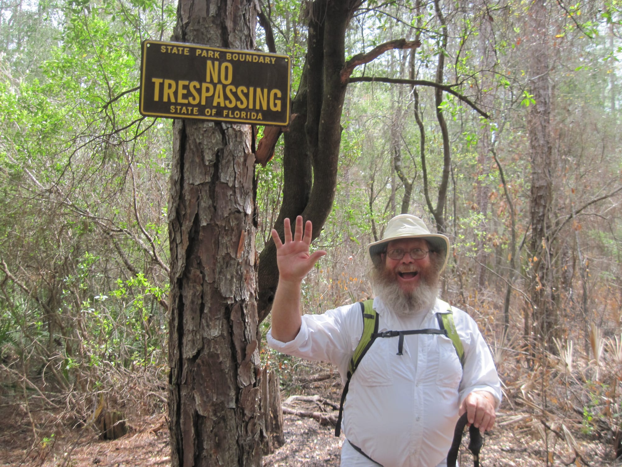 Man with a silly expression under a No Trespassing sign in a forest