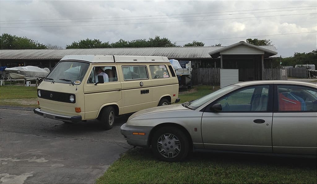 VW camper driving past boats and cars in the rain