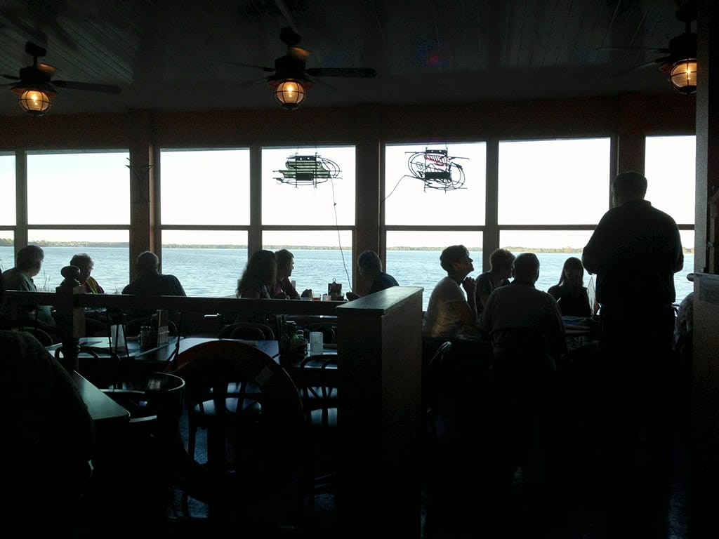 Silhouettes of diners against windows overlooking a lake