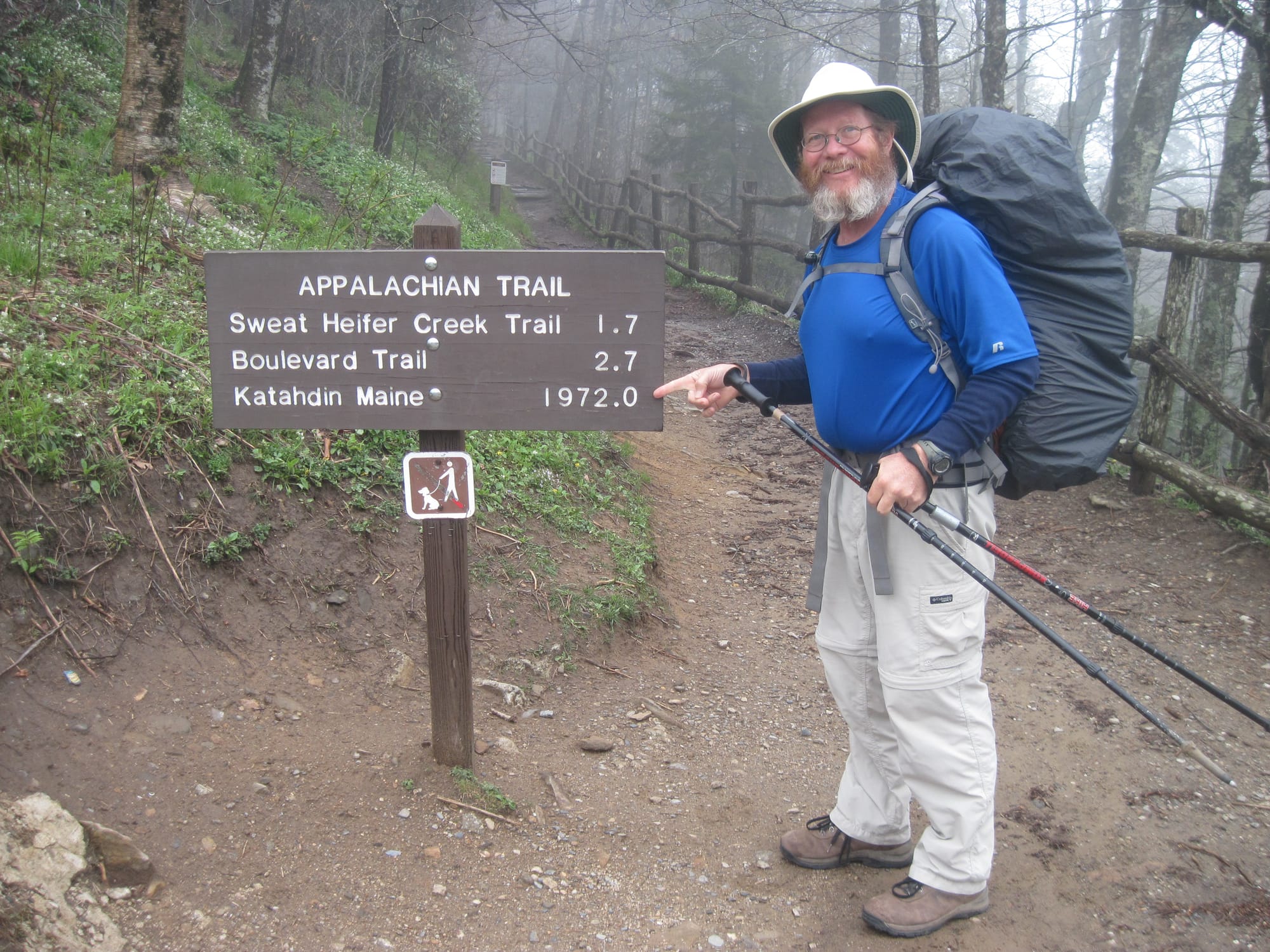 A male backpacker pointing to an AT sign with Katahdin mileage