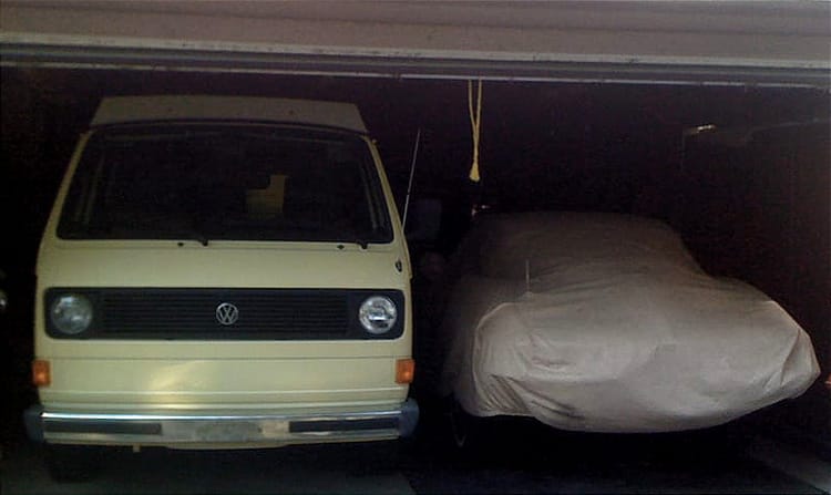 A VW Westfalia looms next to shorter vehicles in a dark garage