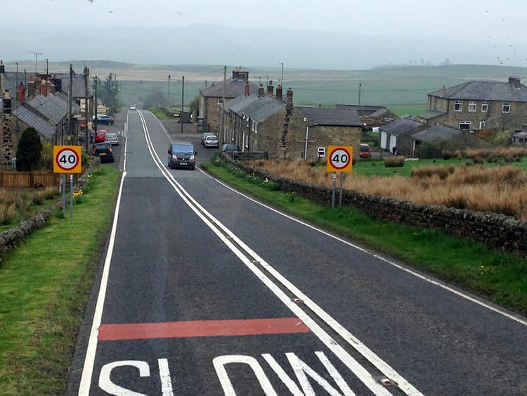 Two lane road through a small rural English village with stone houses