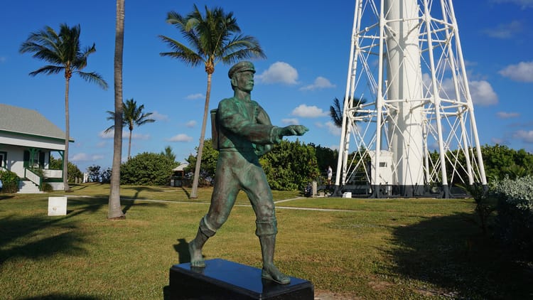 Statue of mailman in old time clothing near base of lighthouse