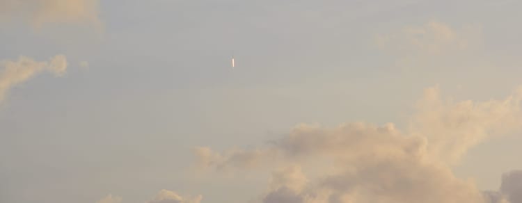 Rocket with streak of flame pointed straight up into a cloudy sky