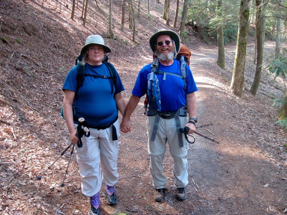 Woman and man backpackers holding hands on a footpath in the woods