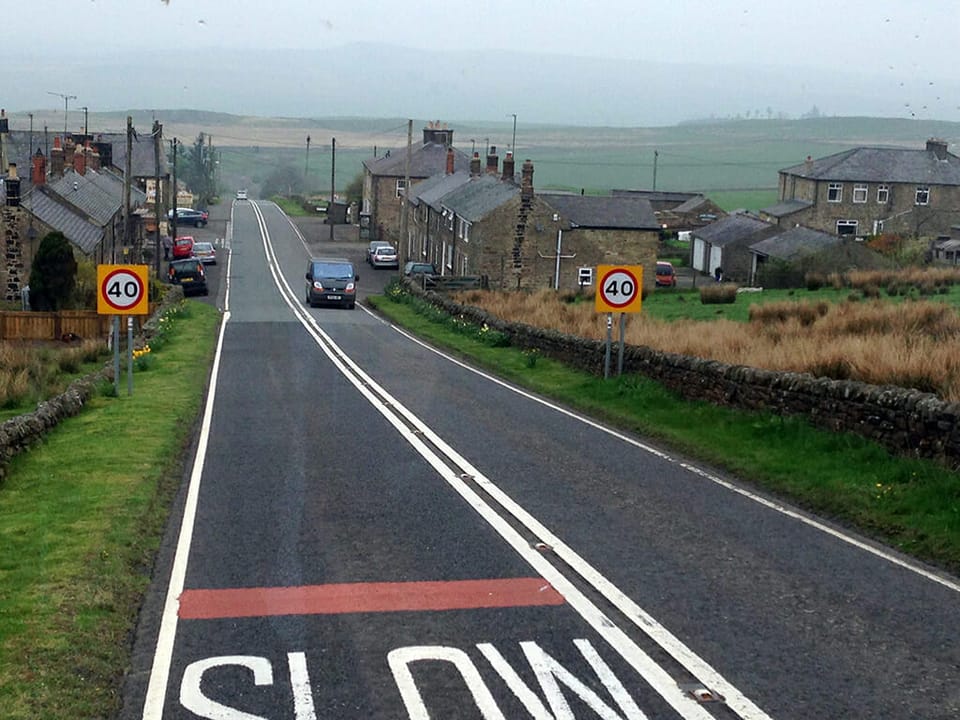 Two lane road through a small rural English village with stone houses
