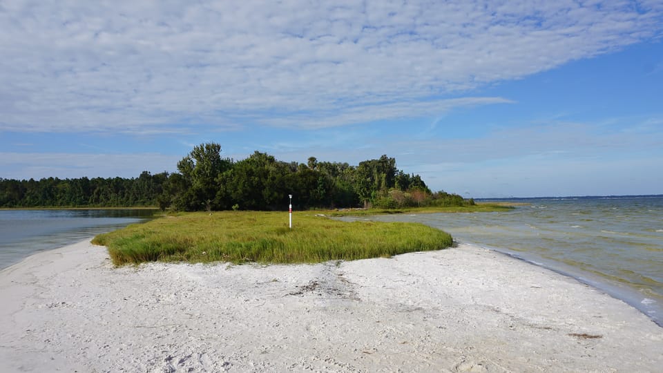 A sandy peninsula with a grassy point at an inlet marked with a post