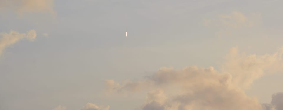 Rocket with streak of flame pointed straight up into a cloudy sky