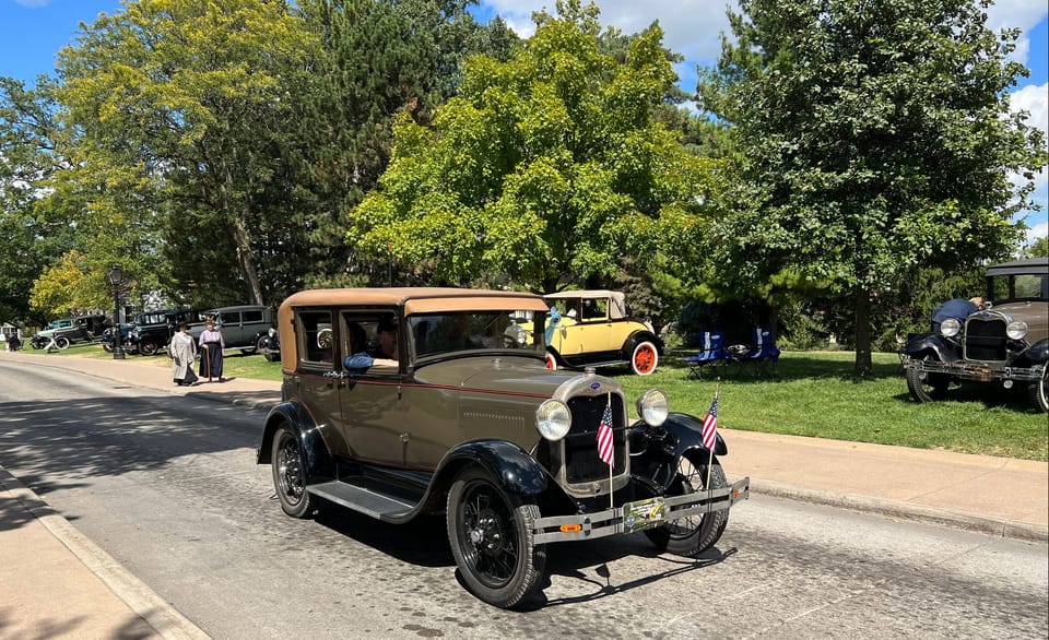 Ford driving a street mottled with oil spots past cars parked under the trees